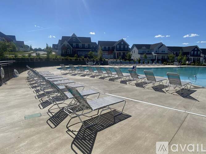 A sunny day at the pool with chairs and a building in the background.