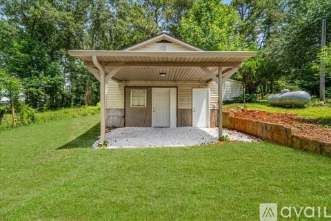 A small house with a porch and a white door is surrounded by greenery.