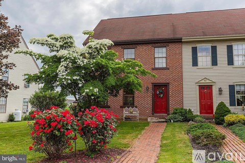 A house with a red door and a red flower bush in front.