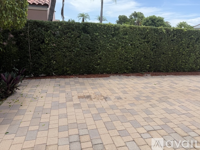 A brick patio is surrounded by a green hedge.