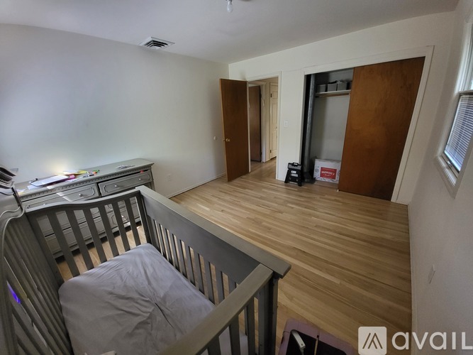 A baby's crib sits in a room with a wooden floor and a doorway leading to another room.