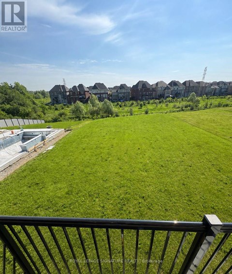 A green field with a fence in the foreground and houses in the background.