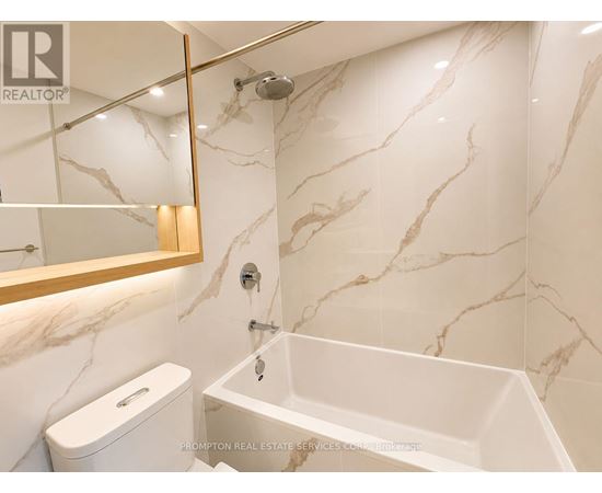 A white toilet sits next to a white bathtub in a marble bathroom.