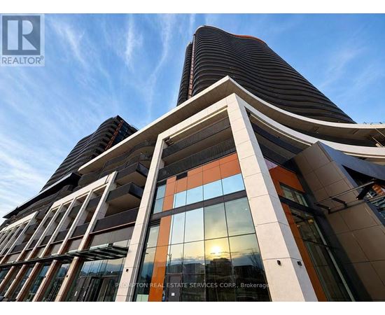 A modern building with a glass facade and a sunset in the background.