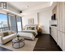 A well-lit bedroom with a large bed, a couch, a coffee table, and a kitchenette.