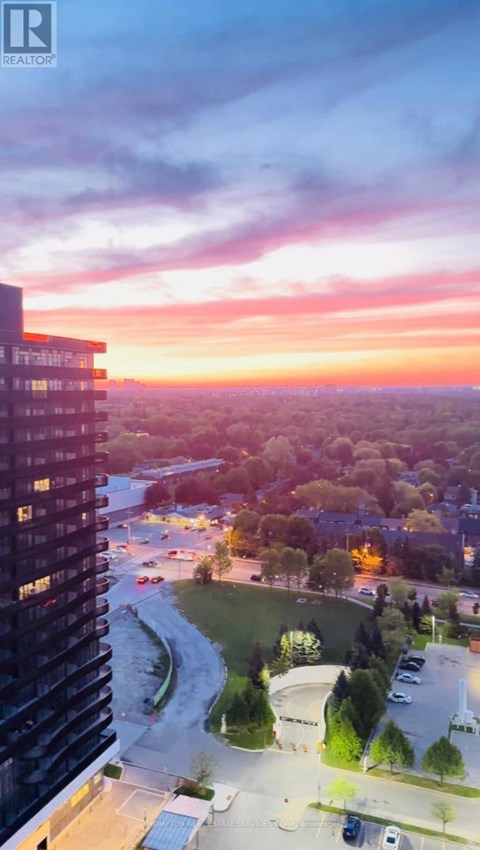 A sunset view from a high-rise building with a parking lot and trees in the foreground.