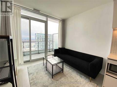 A black sofa sits in a living room with a glass table and a balcony with a view of the city.