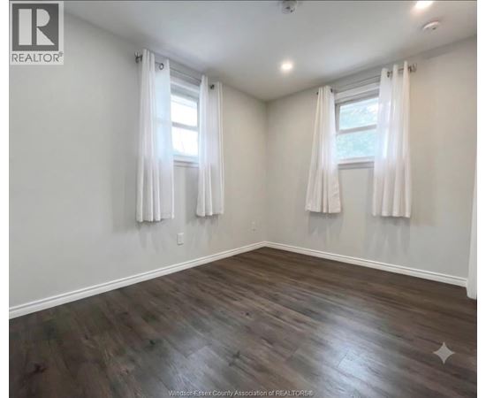 A room with wooden floors and two windows with white curtains.