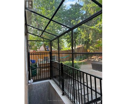 A balcony with a black railing and a glass roof overlooking a backyard.
