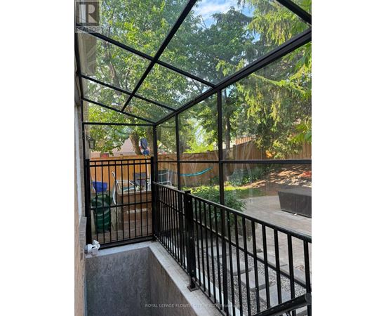 A balcony with a black railing and a glass roof overlooking a backyard.