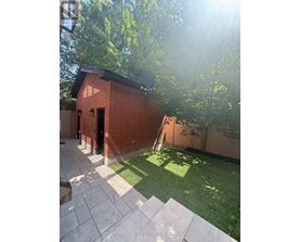 A small red brick building with a black door is surrounded by a green lawn and trees.