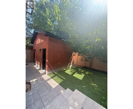 A small red brick building with a black door is surrounded by a green lawn and trees.