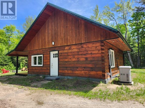 A wooden cabin with a white door and windows is surrounded by trees.
