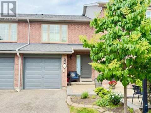 A red brick house with a grey garage door and a tree in front.
