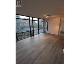 A spacious room with wooden flooring and large windows overlooking a cityscape.
