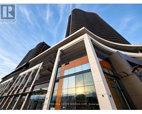 A modern building with a curved glass facade and a sunset in the background.