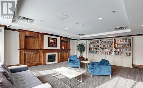 A living room with a grey sofa, a blue armchair, a glass coffee table and a bookshelf filled with books.