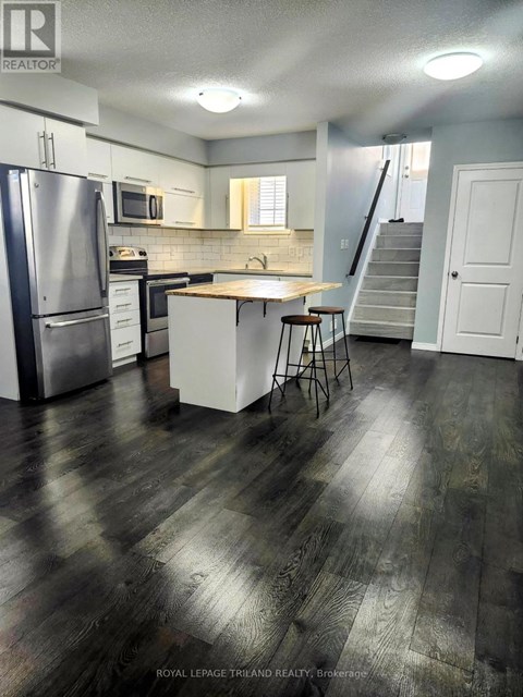 A kitchen with a refrigerator, stove, and bar stools.