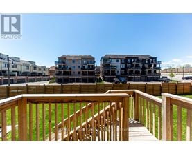A wooden deck with a railing overlooks a grassy area and apartment buildings.
