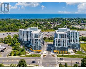 A large, modern building complex with a glass facade is situated in a parking lot with a view of the ocean in the distance.