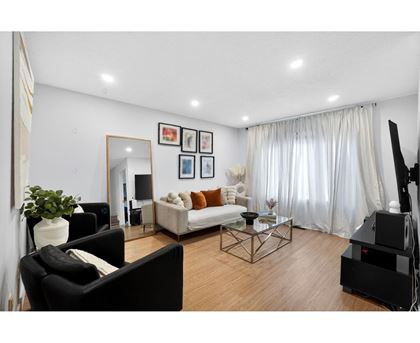 A living room with a black couch, a white sofa, a glass coffee table, and a TV.