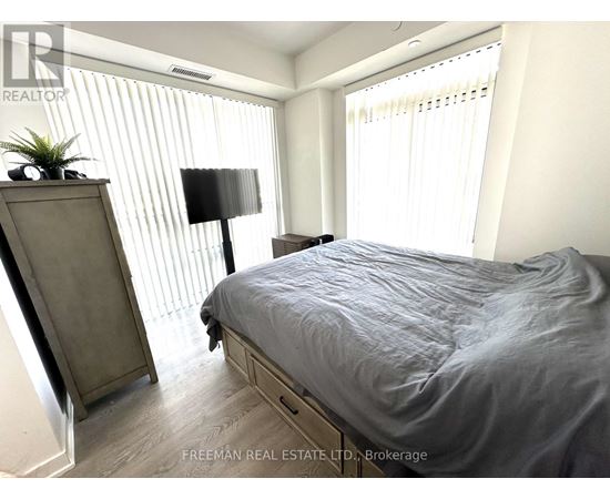 A bedroom with a bed, nightstand, and a plant on a dresser.
