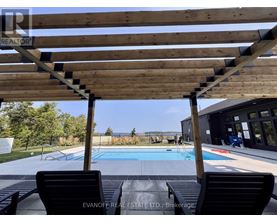 A wooden pergola over a pool with two black chairs underneath.