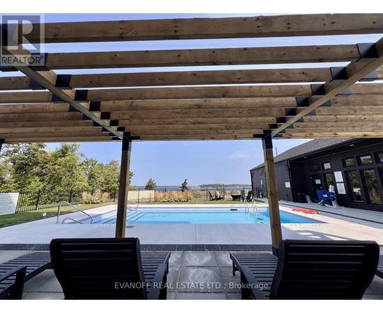 A wooden pergola over a pool with two black chairs underneath.