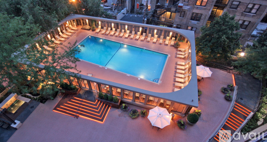 A large outdoor swimming pool surrounded by a patio area with lounge chairs and umbrellas.