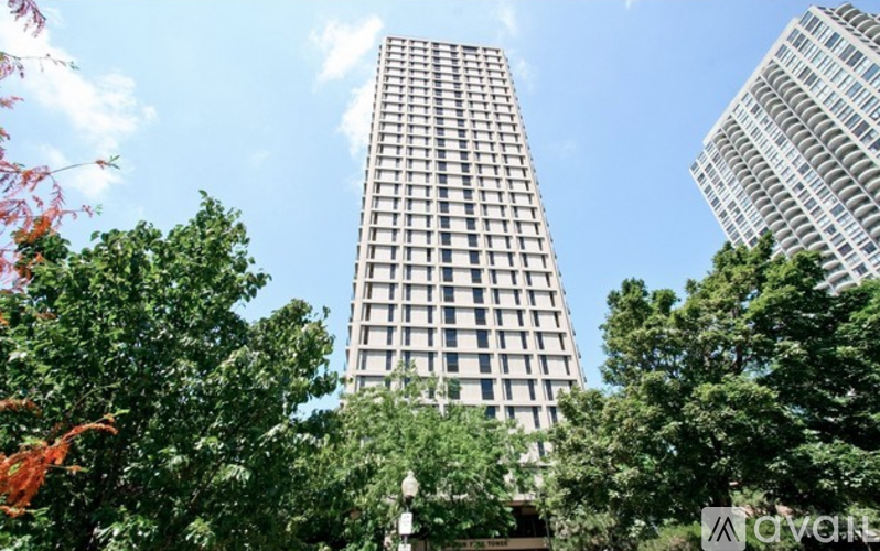 A tall building stands in front of a skyline with trees in the foreground.