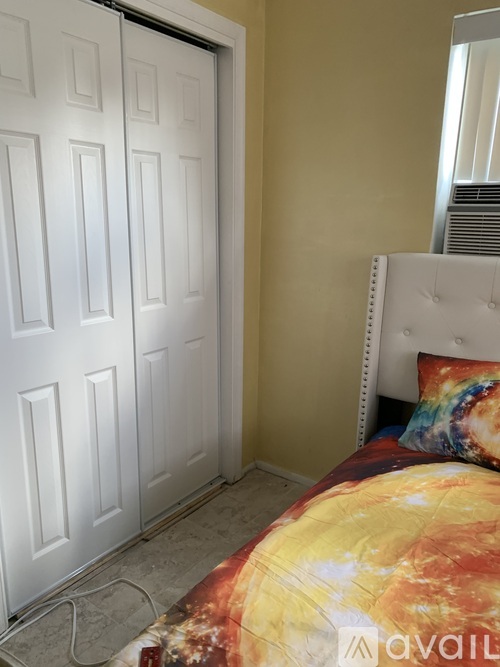 A white door is on the left of a bed with a yellow and orange comforter.