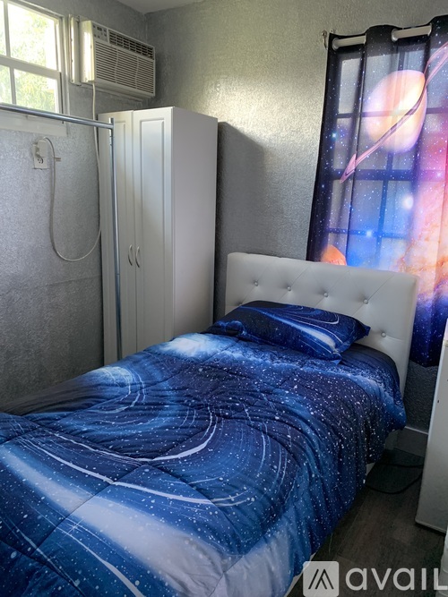 A bed with a blue and white comforter is in a room with a window and a white headboard.