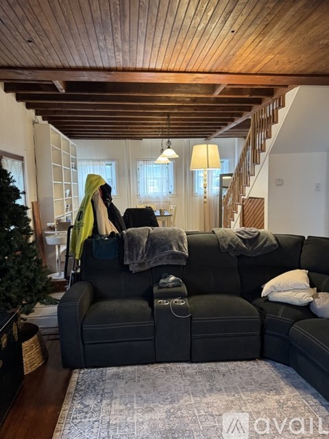 A woman is standing in a living room with a black couch and a Christmas tree.