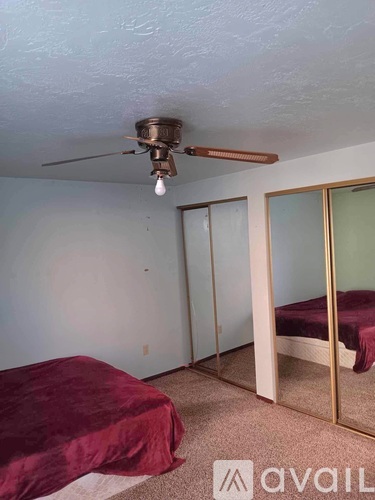 A bedroom with a ceiling fan and a bed with a burgundy cover.