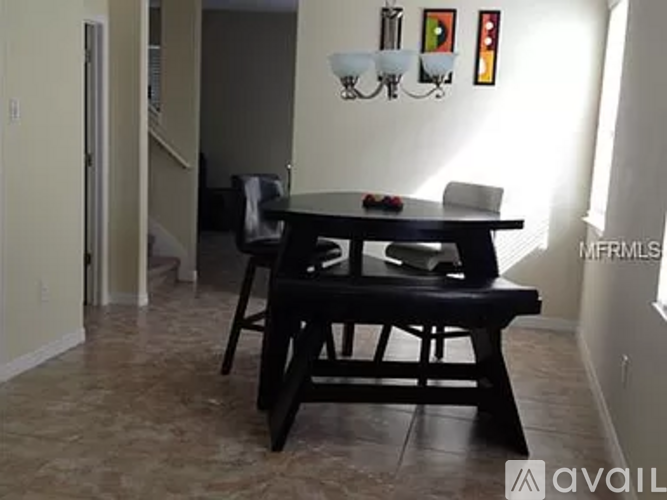 A black dining table with four chairs is in a room with a white wall and a chandelier.