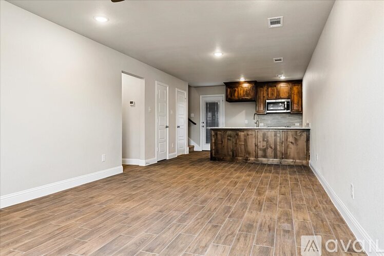 A spacious room with wooden flooring and a kitchen area with a microwave.