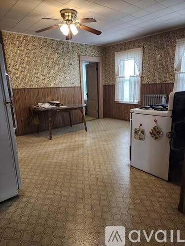 A kitchen with a refrigerator, a table, and a ceiling fan.