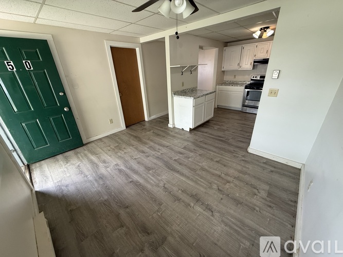 A room with a green door and a kitchen area with white appliances.