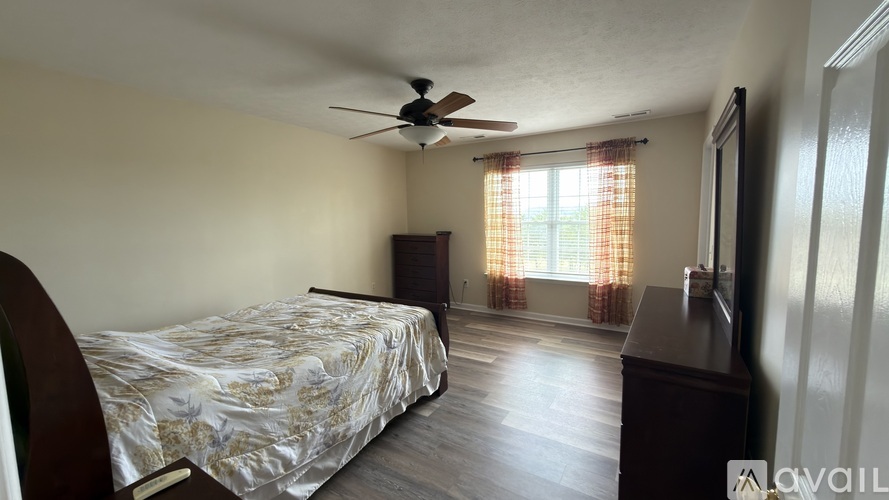 A bedroom with a bed, dresser, and window with curtains.