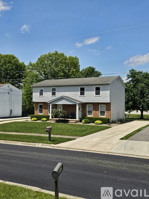 A house with a white exterior and a grey roof is surrounded by greenery and a clear sky.