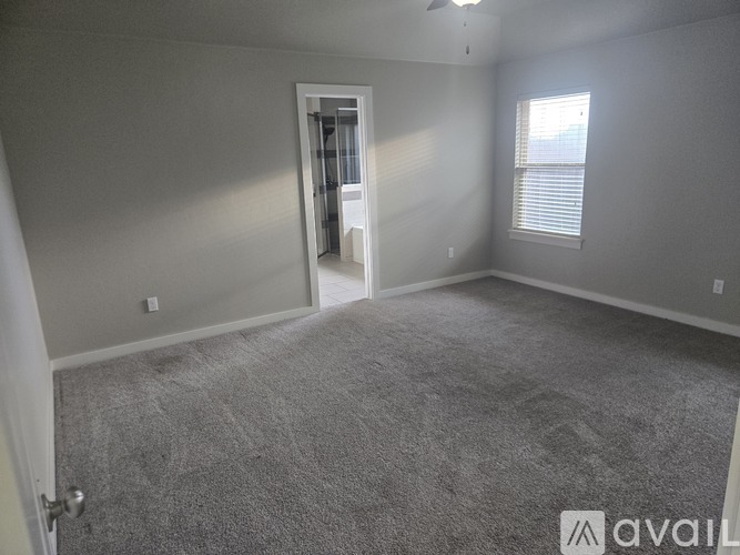 A spacious room with grey carpeting and a door leading to another room.
