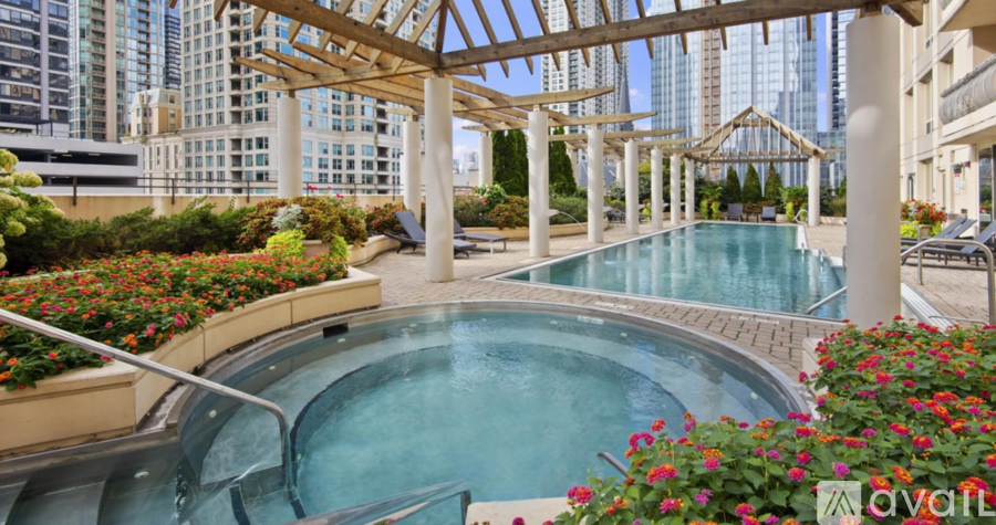 A hot tub sits in the middle of a patio with a pool and flowers.
