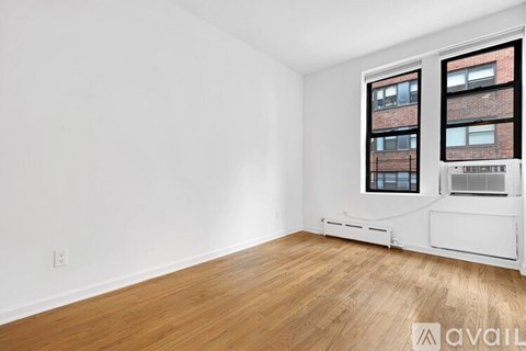 A room with wooden flooring and a window overlooking a brick building.
