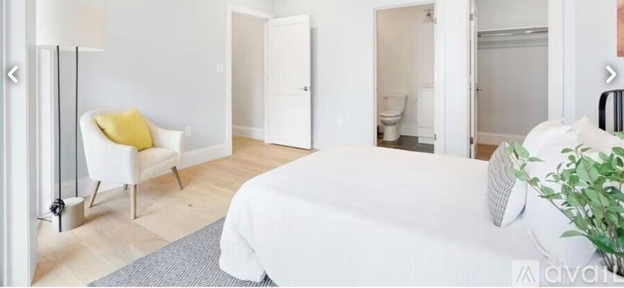 A white bedroom with a bed, chair, and plant.