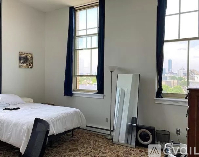 A bedroom with a bed, chair, and a window with a view of the city.