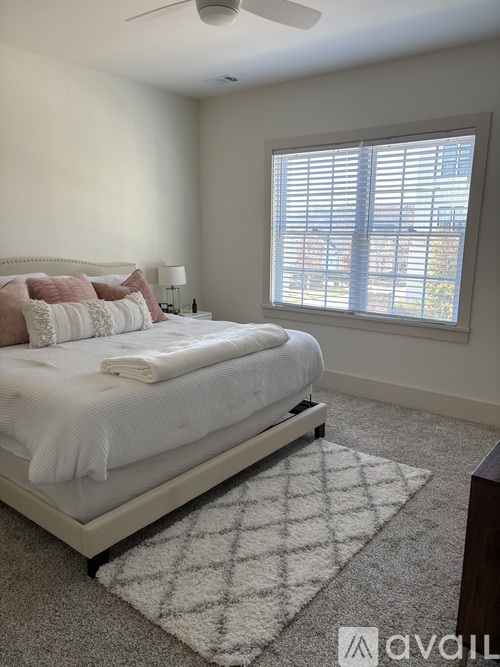 A bedroom with a neatly made bed and a window with blinds.