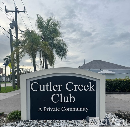 A sign for Cutler Creek Club, a private community, is displayed in front of some palm trees.
