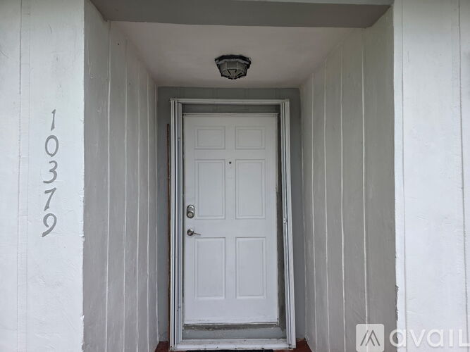 A white door is in the center of a white wall with the number 10379 on the left.