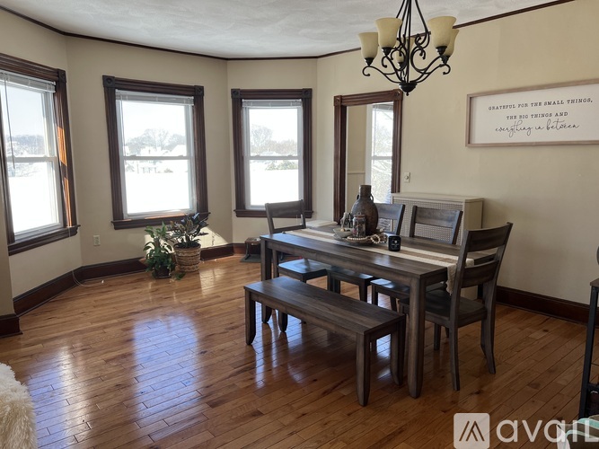 A dining room with a wooden table and bench, a chandelier, and a framed quote on the wall.