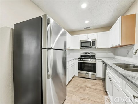 A kitchen with a black refrigerator, stainless steel appliances, and wooden flooring.